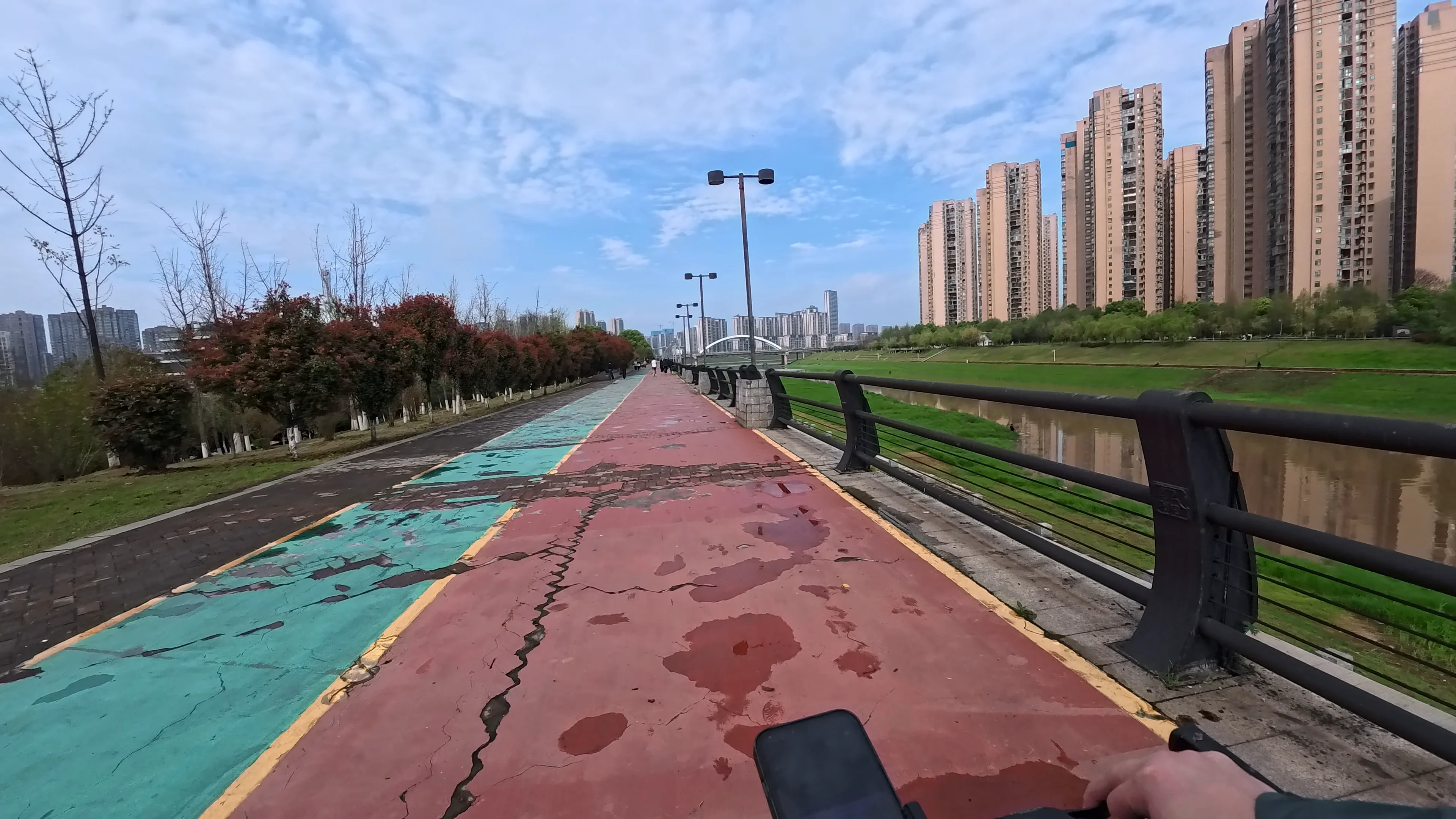 Peaceful riverside cycling route with colorful lanes, high-rise apartments and urban skyline views in Changsha POV cycling along a colorful riverside bike path beside modern residential towers in Changsha, China after light rain
